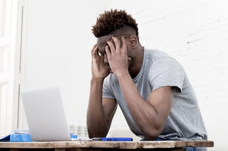 stressed_employee_at_his_desk_holding_head wellness wellbeing mental health coping strategies calm balance unhappy anxiety