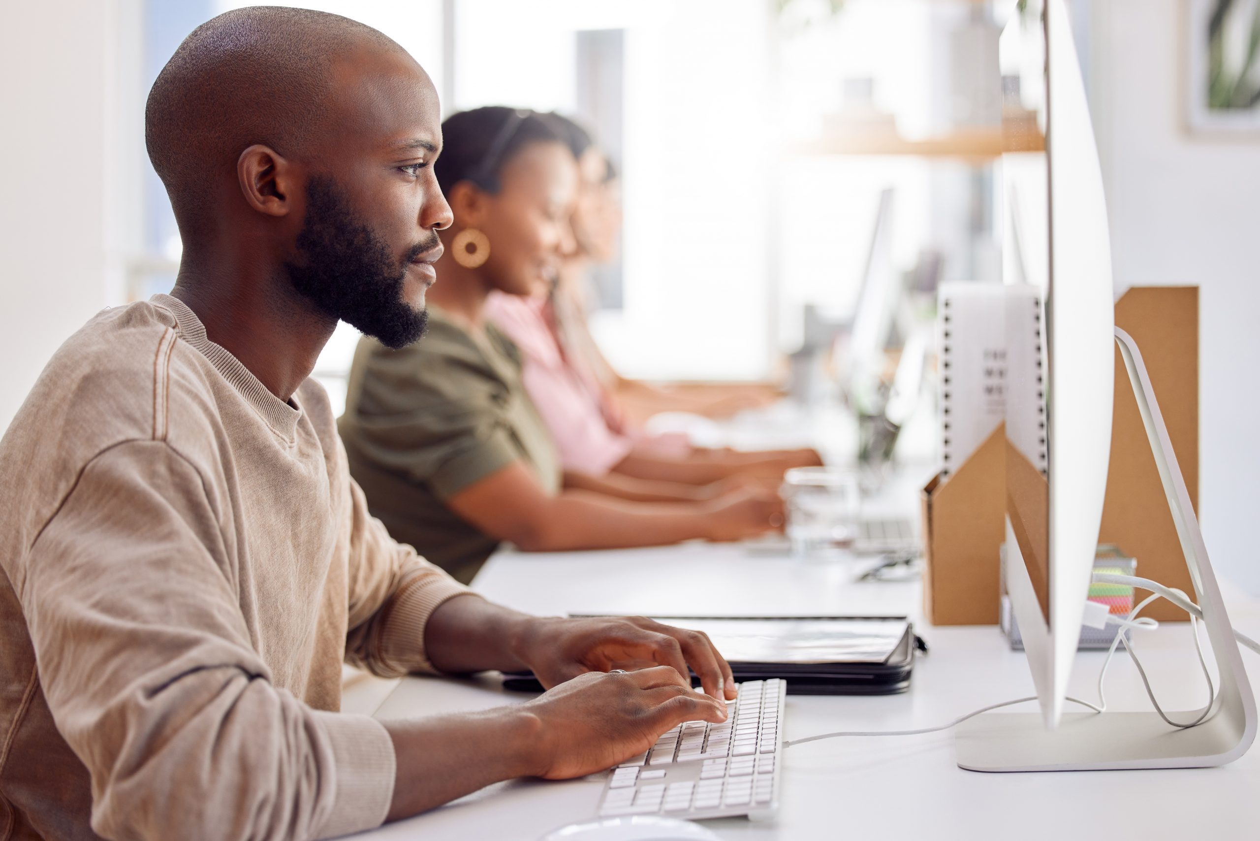 Shot of a businessman working on his computer while his colleagues sit in the background and work readiness