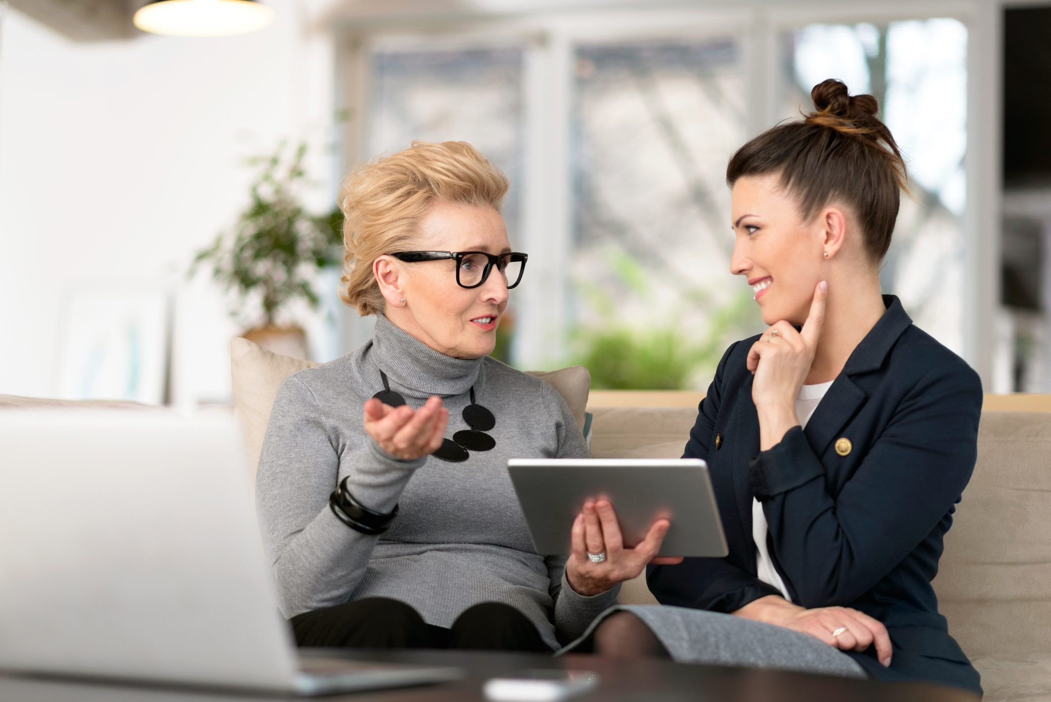 Happy young woman talking with her senior mentor Senior woman talking with young businesswoman, using digital tablet, sharing experience, senior women menopause retirement