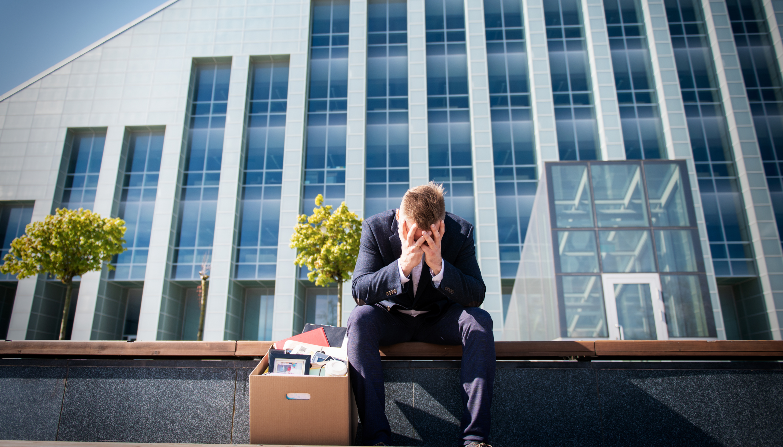a sad employee sitting outside a business building after being dismissed in a dismissal legal dispute resulting in job termination or being fired where he has to leave the company