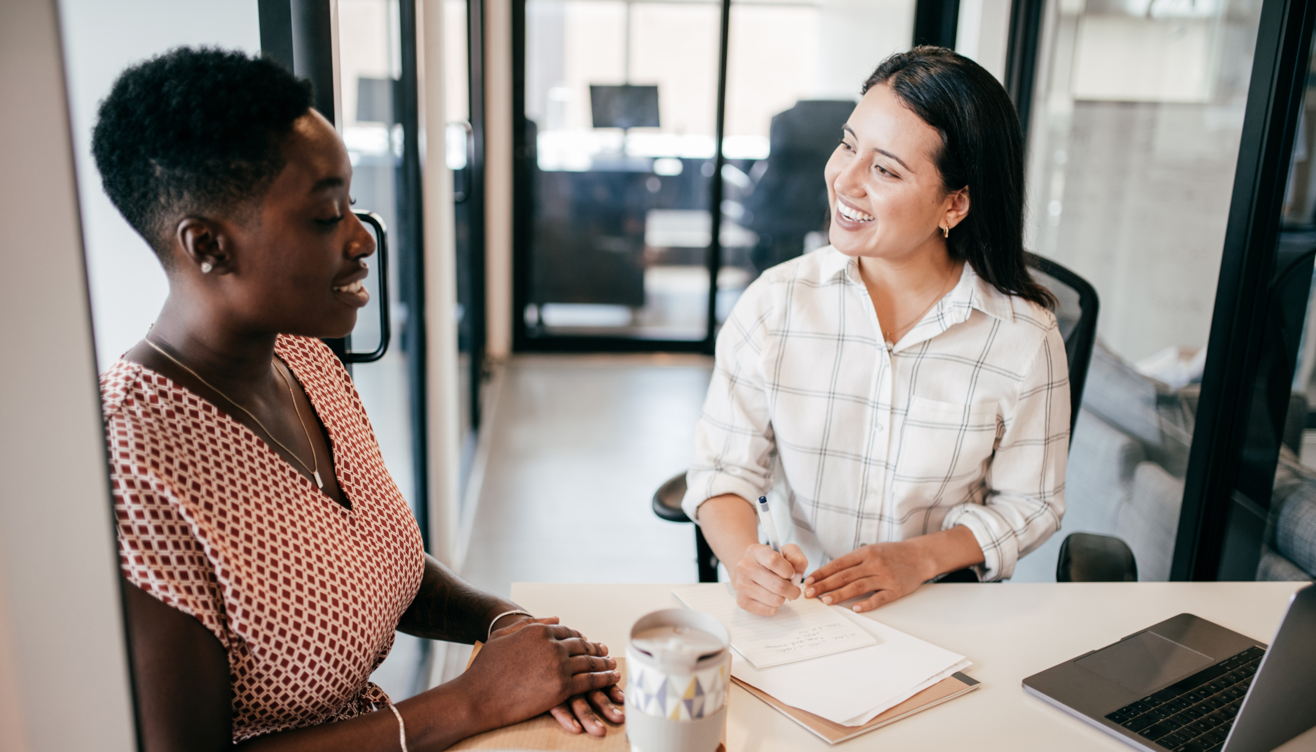 hiring and recruitment methods based on skills based hiring when considering job candidate CVs and resumes where two ladies are chatting at a table in a work environment