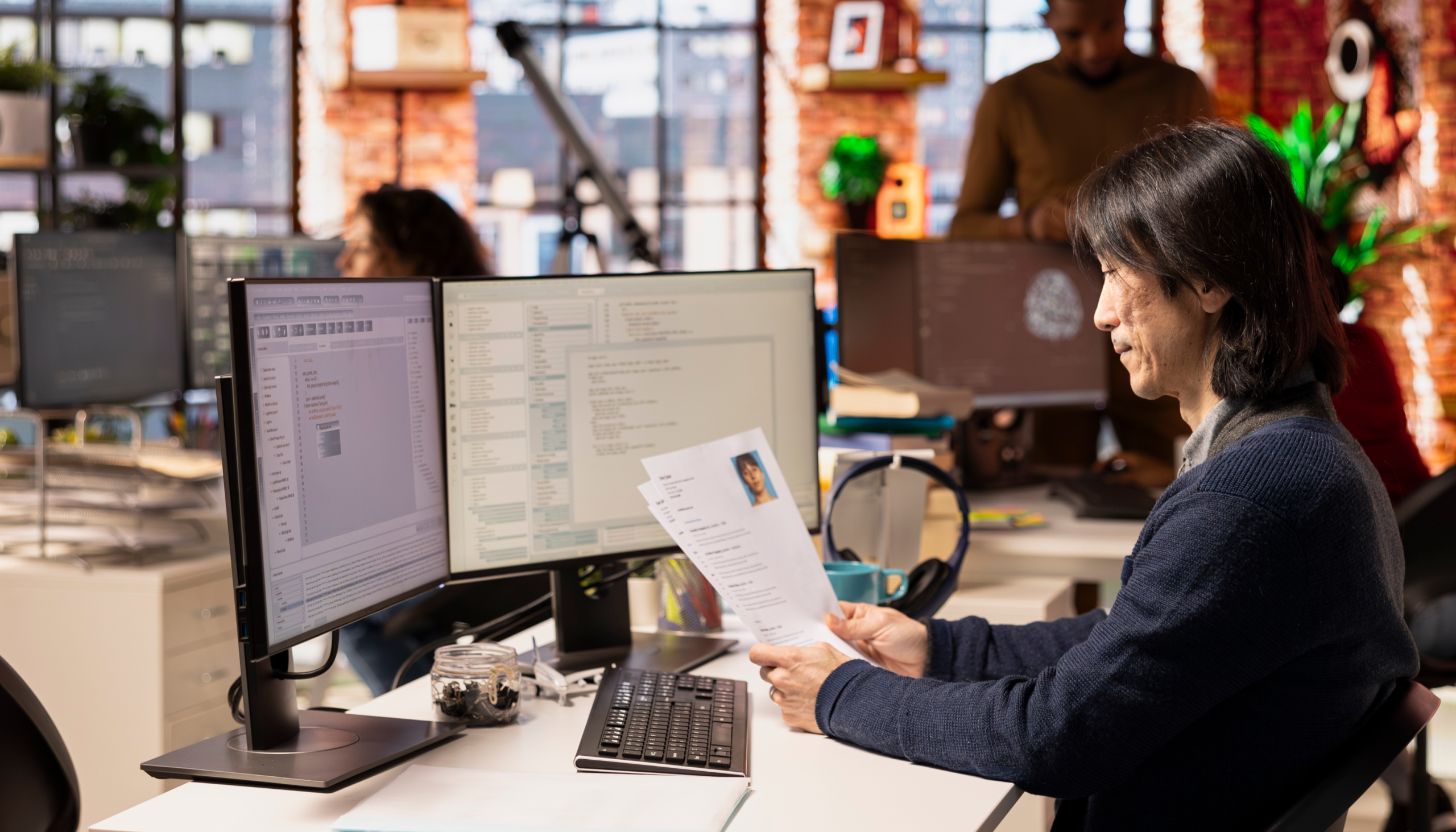 employee looking at resumes and CVs for a job position while looking at coding on computer tech screens in the workplace