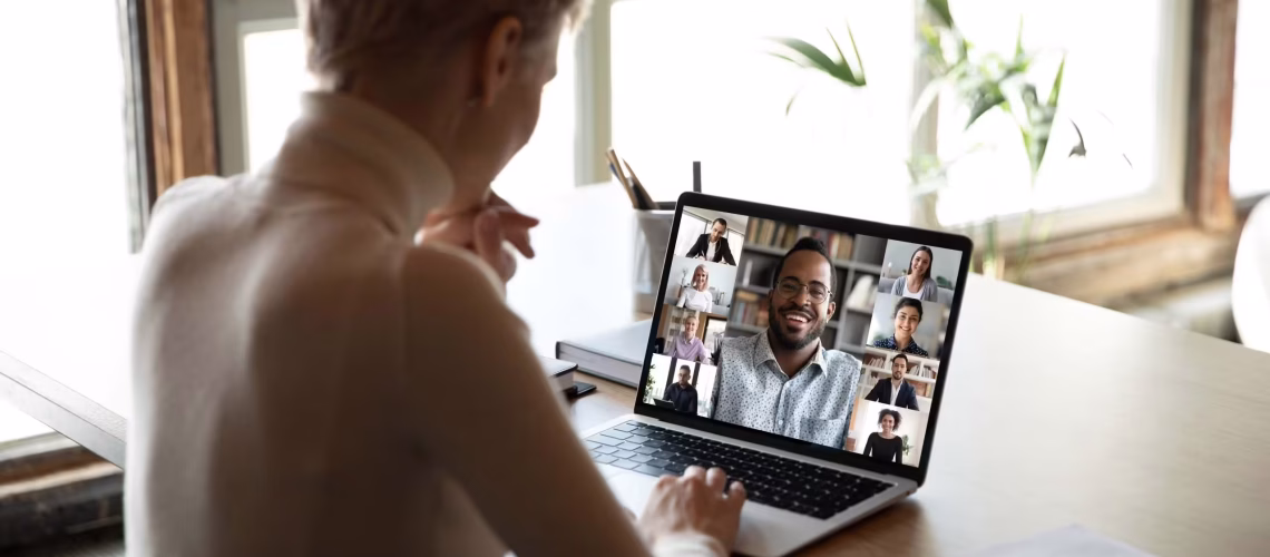 Woman sitting at workplace desk taking part at group on-line meeting using webcam laptop and videoconferencing app, view over female shoulder. Modern tech, distant webinar, online negotiations concept remote work engagement hr tech