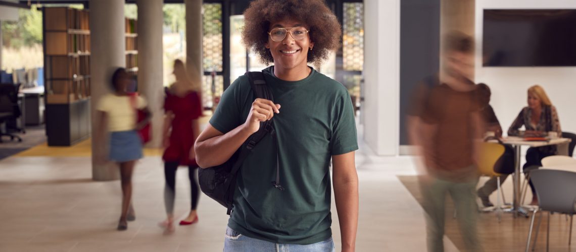 Portrait Of Smiling Male Student In Busy University Or College Building