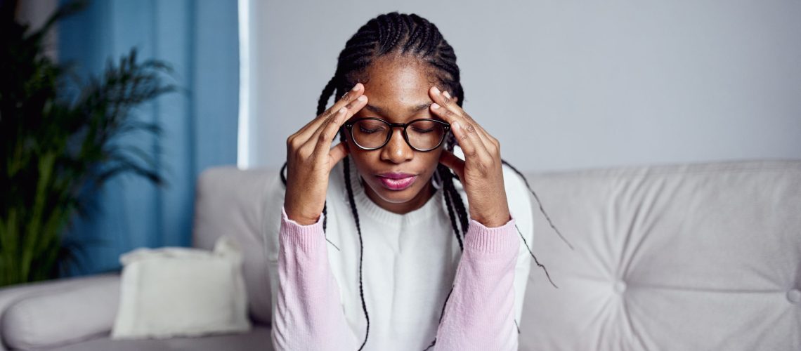 A young girl is sitting on the couch at home with her head in her hands GettyImages-1356562872 - Medihelp - stress well-being wellbeing wellness burnout tired