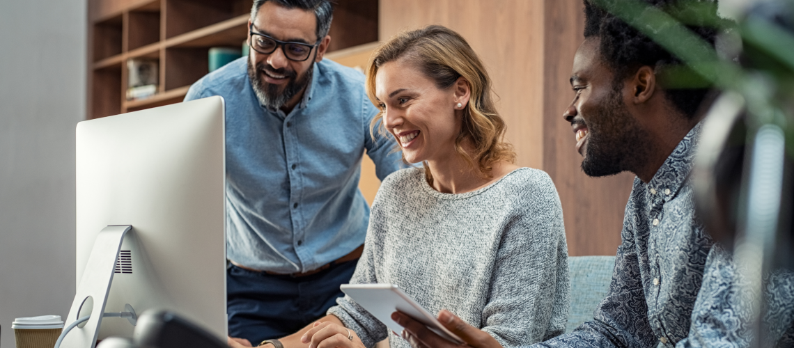 a team of employees talking together at a laptop showing a strong and happy company culture