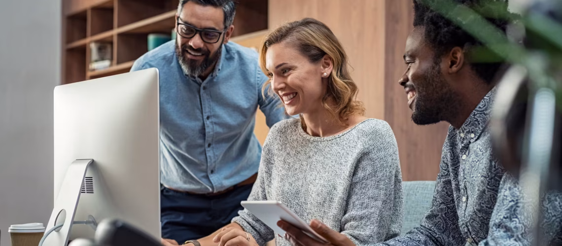 a team of employees talking together at a laptop showing a strong and happy company culture