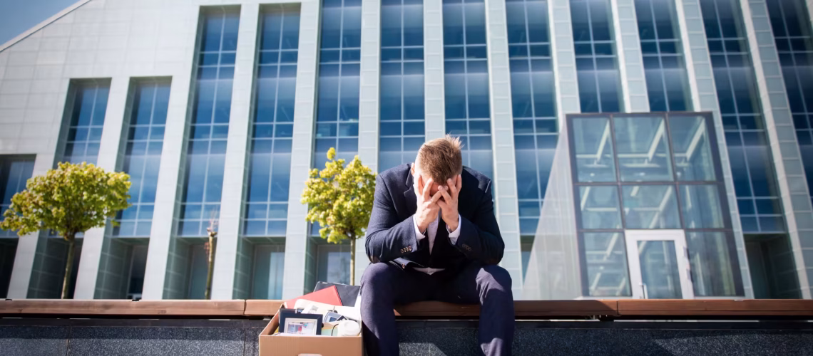 a sad employee sitting outside a business building after being dismissed in a dismissal legal dispute resulting in job termination or being fired where he has to leave the company